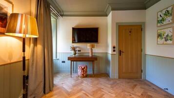 Een kamer met een visgraatvloer, een houten deur, een tafel met een vaas en een lamp.