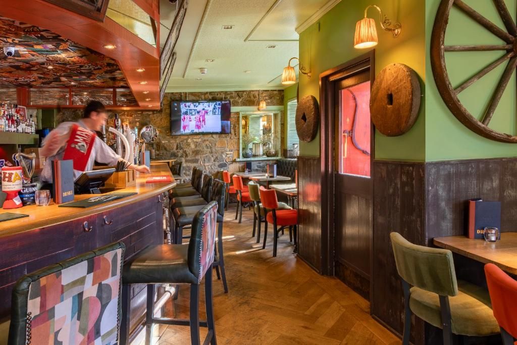 Zona de bar con un cantinero, múltiples opciones de asientos, incluyendo cabinas y mesas, y una pantalla de televisión montada en la pared.