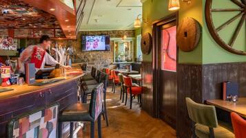 Zona de bar con un cantinero, múltiples opciones de asientos, incluyendo cabinas y mesas, y una pantalla de televisión montada en la pared.