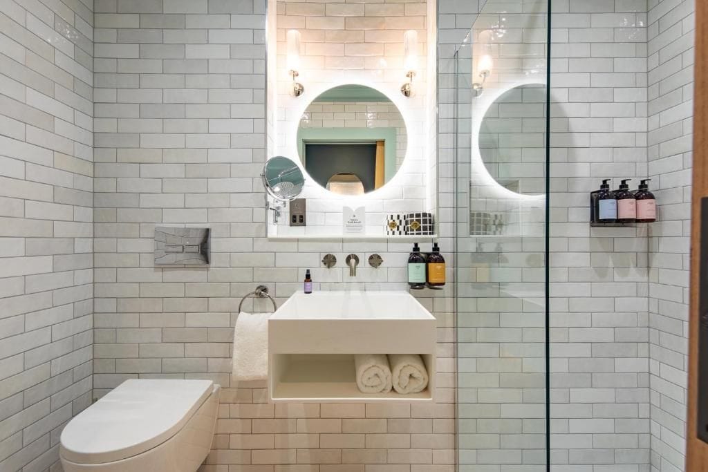 Un baño moderno con inodoro, lavabo con espejo y cabina de ducha de vidrio.