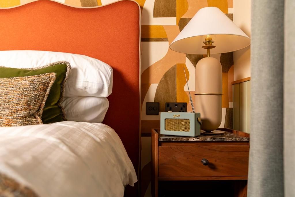 Een net opgemaakt bed met kussens, een bedlampje en een radio op een houten nachtkastje.