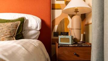 Een net opgemaakt bed met kussens, een bedlampje en een radio op een houten nachtkastje.