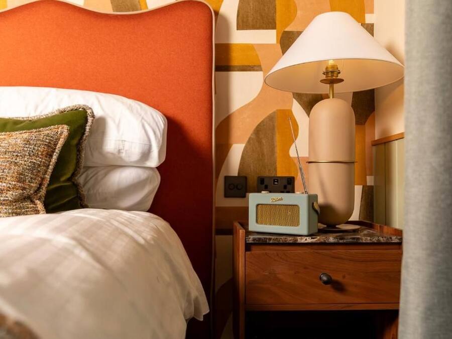 A neatly made bed with pillows, a bedside lamp, and a radio on a wooden nightstand.