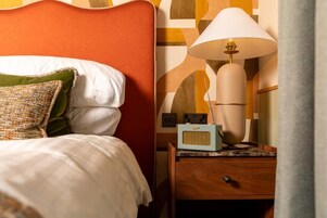 Una cama bien hecha con almohadas, una lámpara de noche y una radio sobre una mesita de madera.