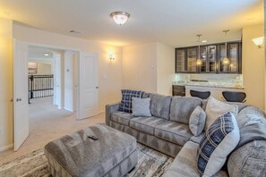 A living room with a grey sectional sofa, ottoman, and a kitchen area with cabinets and a countertop. - Spacious 4BR Richmond Home w/ Game & Media Room (Richmond)