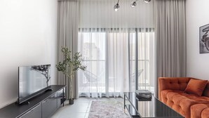 A modern living room with a flat-screen TV, a sofa, a glass coffee table, and a large window with sheer curtains. - Sahab - Sunset 1BR at Al mamsha Sharjah (Sharjah)