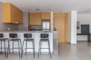 Een moderne keuken met houten kastjes, een roestvrijstalen koelkast en een bargedeelte met vier krukken.