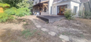 A modern house with a covered patio, a wooden deck, and a stone pathway leading to the entrance. - Large family apart with garden, close to the beach (Arcachon)