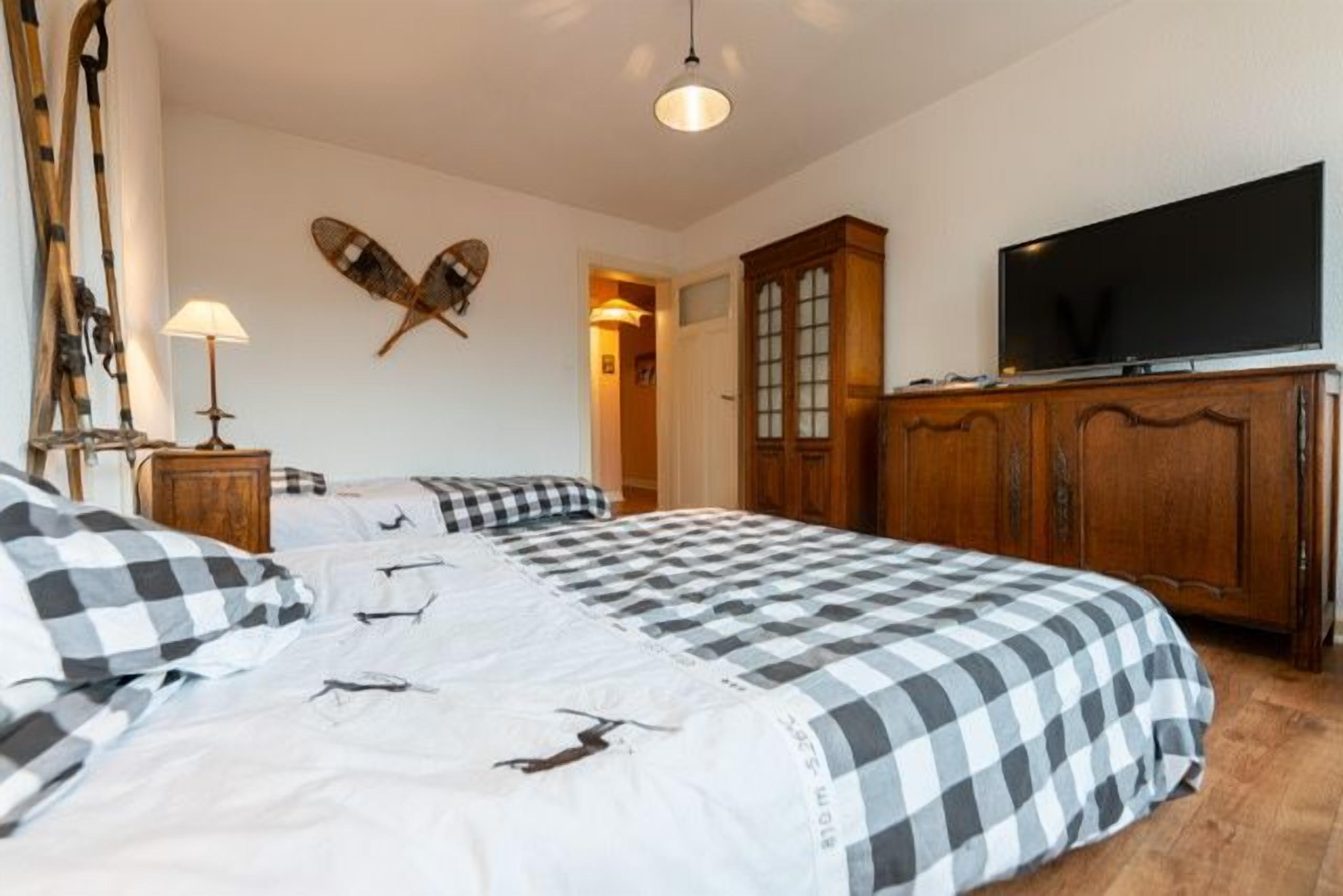 A bedroom with a bed, a television, a wardrobe, and a pair of skis leaning against the wall.
