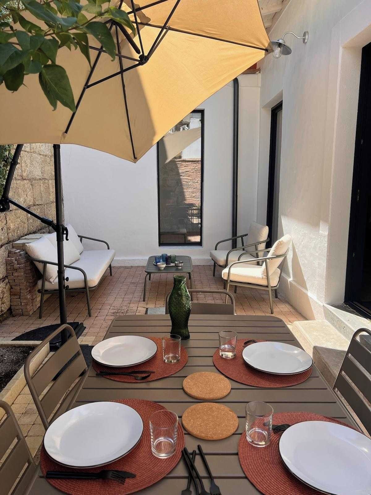 An outdoor dining area with a table set for four, surrounded by chairs, under a large umbrella.