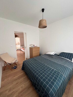 Un dormitorio con cama, cómoda, silla y lámpara colgante.