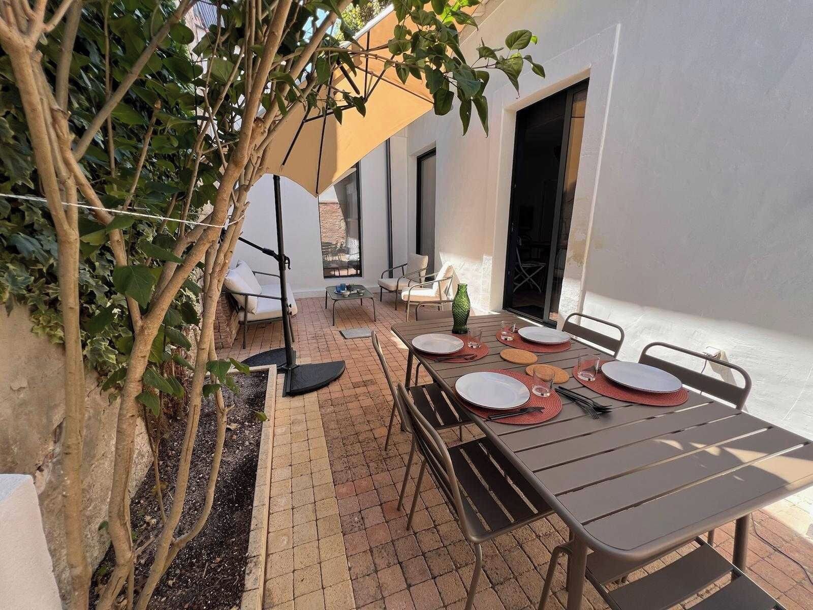 An outdoor patio with a table set for dining, surrounded by chairs, a hanging chair, and a potted plant.