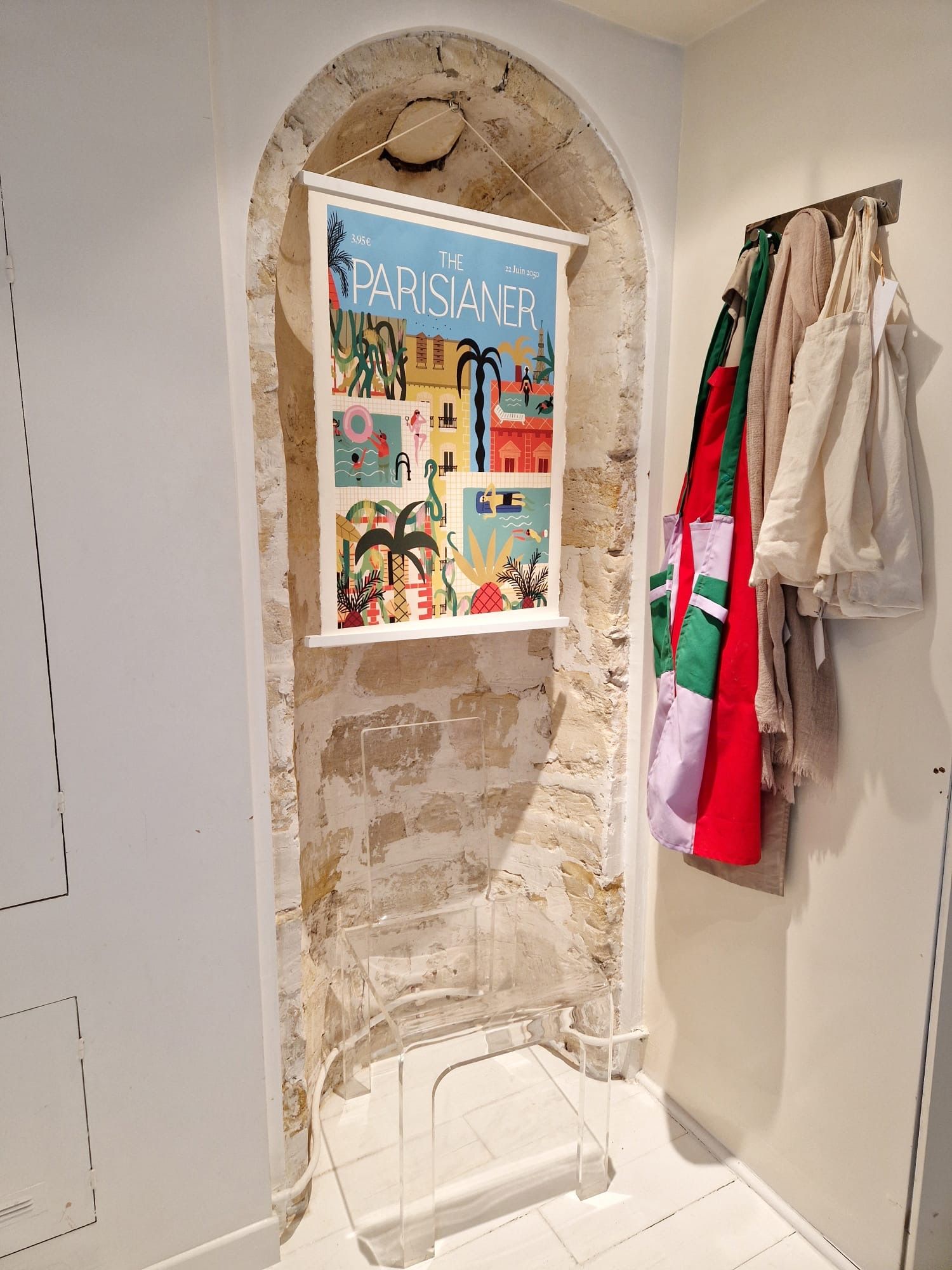 A room with a poster of 'The Parisian' magazine, a stone archway, and a rack of clothes.