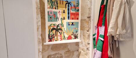 A room with a poster of 'The Parisian' magazine, a stone archway, and a rack of clothes.