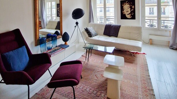 Ein Wohnzimmer mit freiliegenden Holzbalken, einem weißen Sofa, einem roten Sessel, einem Glastisch und einem großen Spiegel.