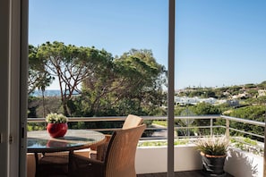 A balcony with wicker furniture, a glass table, and potted plants. - Vrbo Property (Faro)