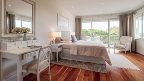 Ein Schlafzimmer mit Bett, Schreibtisch, Stuhl, einem großen Spiegel und Blick ins Freie.