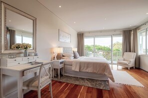 A bedroom with a bed, a desk, a chair, a large mirror, and a view of the outdoors. - Vrbo Property (Faro)