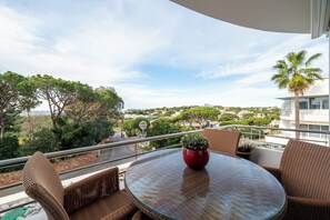 A balcony with wicker furniture, a glass table, and a red vase. - Vrbo Property (Faro)