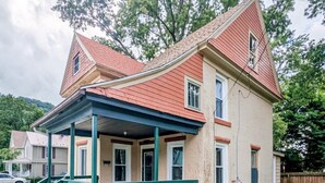 A two-story house with a red roof, a porch with green railings, and a brick exterior. - Warren Wilderness - A Unique Architectural Gem Near the Allegheny River and Kinzua Dam (Warren)