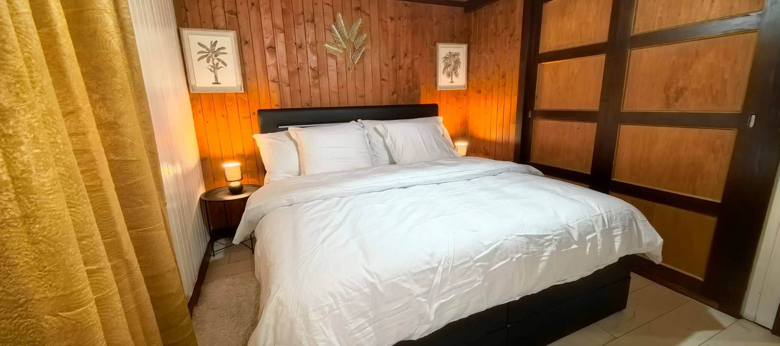 Een net opgemaakt bed met witte lakens in een kamer met houten paneelwanden en een deur met een gecentreerd paneelpatroon.