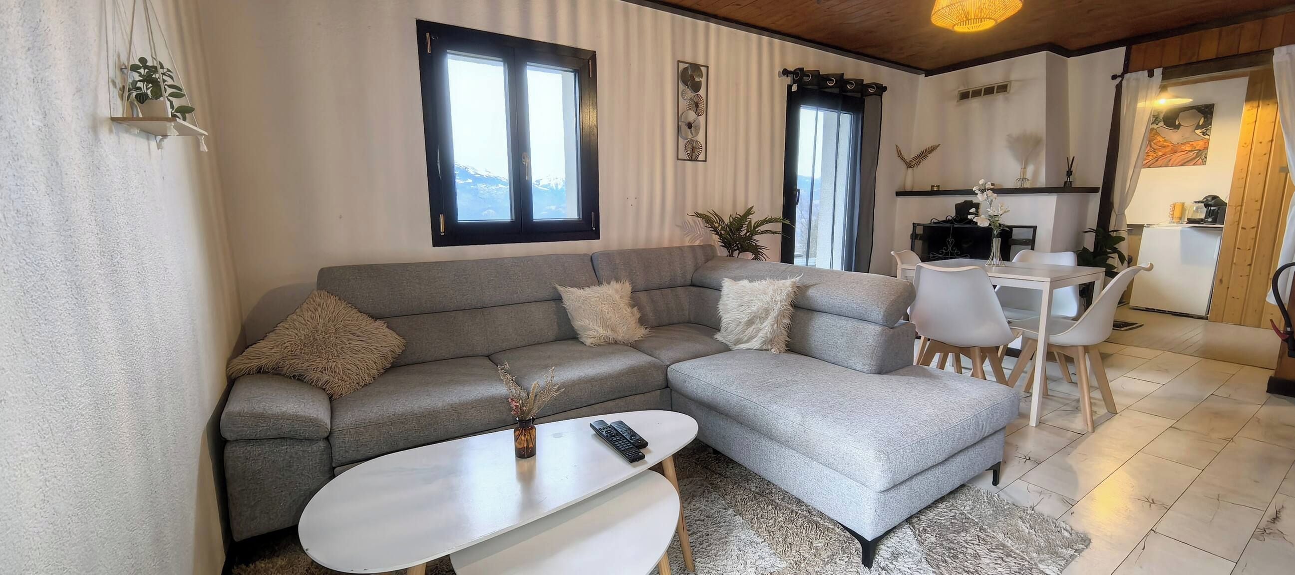 Una sala moderna con un sofá seccional gris, una mesa de centro blanca y un comedor con una mesa y sillas blancas.