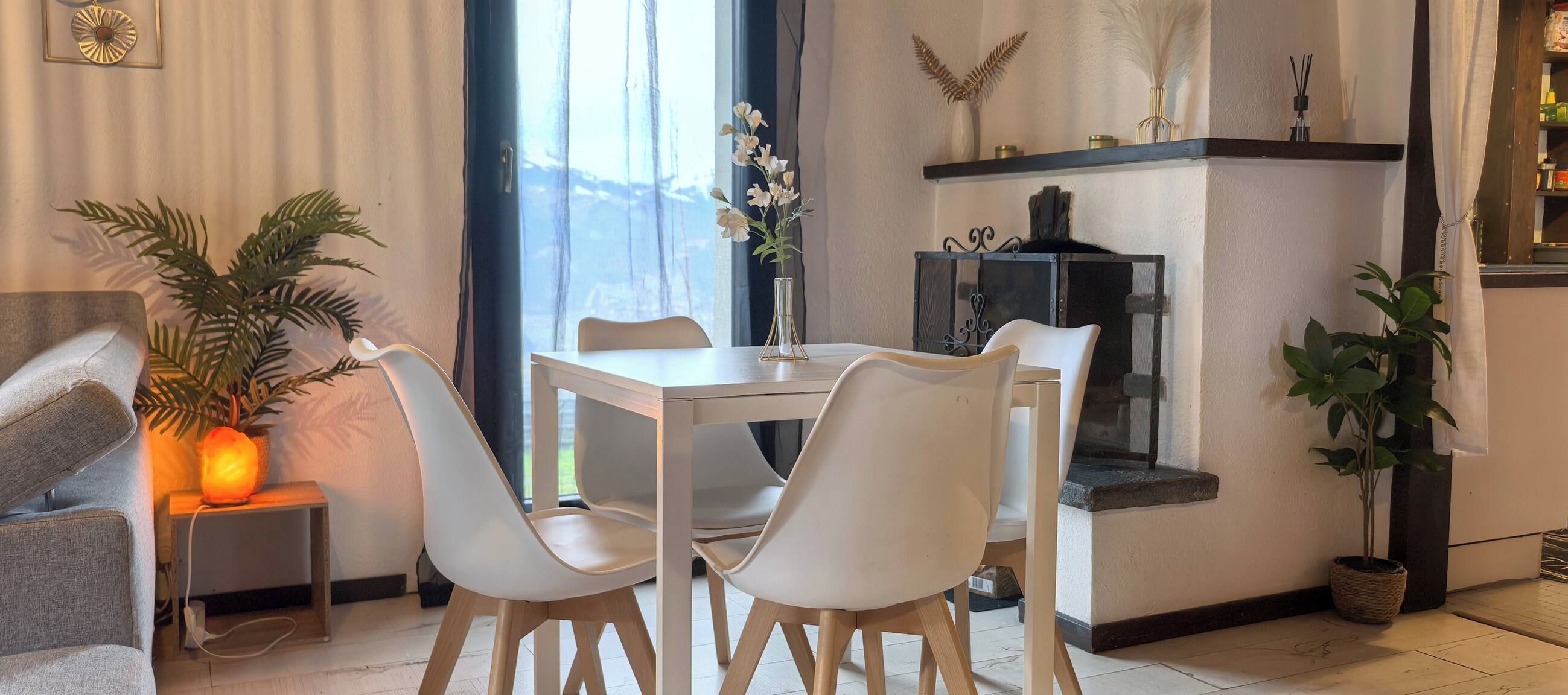 A modern living room with a dining table, two chairs, a sofa, a heater, a potted plant, and a fireplace.