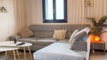 Una sala de estar con un sofá gris, una mesa de centro blanca y una mesita de noche con una lámpara.