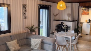 Ein gemütliches Wohnzimmer mit einem grauen Sofa, einem weißen Esstisch mit Stühlen und einer hängenden Leuchte.