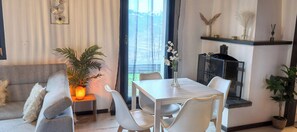 A modern living room with a sofa, a dining table with chairs, a potted plant, and a fireplace. - Chalet L'appel Giettes (Monthey)