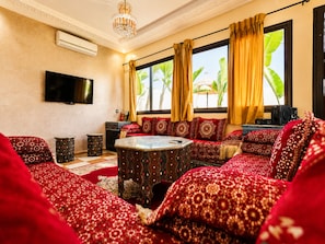 A living room with a sofa set, a coffee table, a flat-screen TV, and a window with curtains.
