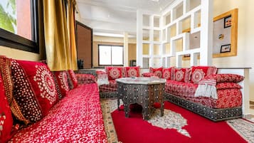 Ein geräumiges Wohnzimmer mit einem roten, gemusterten Sofagarnitur, einem runden Couchtisch und einem dekorativen Teppich.