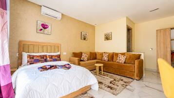 Ein modernes Schlafzimmer mit einem Bett, einer Couch, einem kleinen Tisch und einer Klimaanlage.