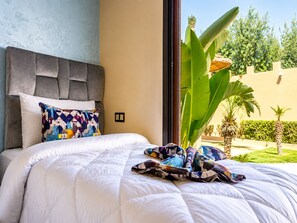 Habitación de hotel con cama, cabecera tapizada en gris, almohada colorida y vistas a zonas verdes.