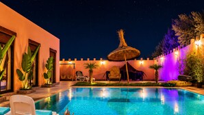 Ein Schwimmbecken mit Liegestühlen und einem Tisch, umgeben von einer Zierwand und Pflanzen.