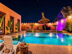 Una piscina con sillas de descanso y una mesa, rodeada por un muro decorativo y plantas.