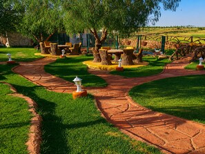 Un jardín ajardinado con un sendero serpenteante, troncos de árboles y mobiliario exterior.