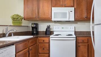 A kitchen with wooden cabinets, a white microwave, a stove, and a dishwasher.