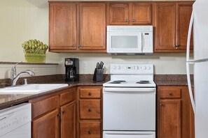 Une cuisine avec des meubles en bois, un micro-ondes blanc, une cuisinière et un lave-vaisselle.