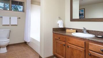 A bathroom with a toilet, sink, vanity, and mirror.