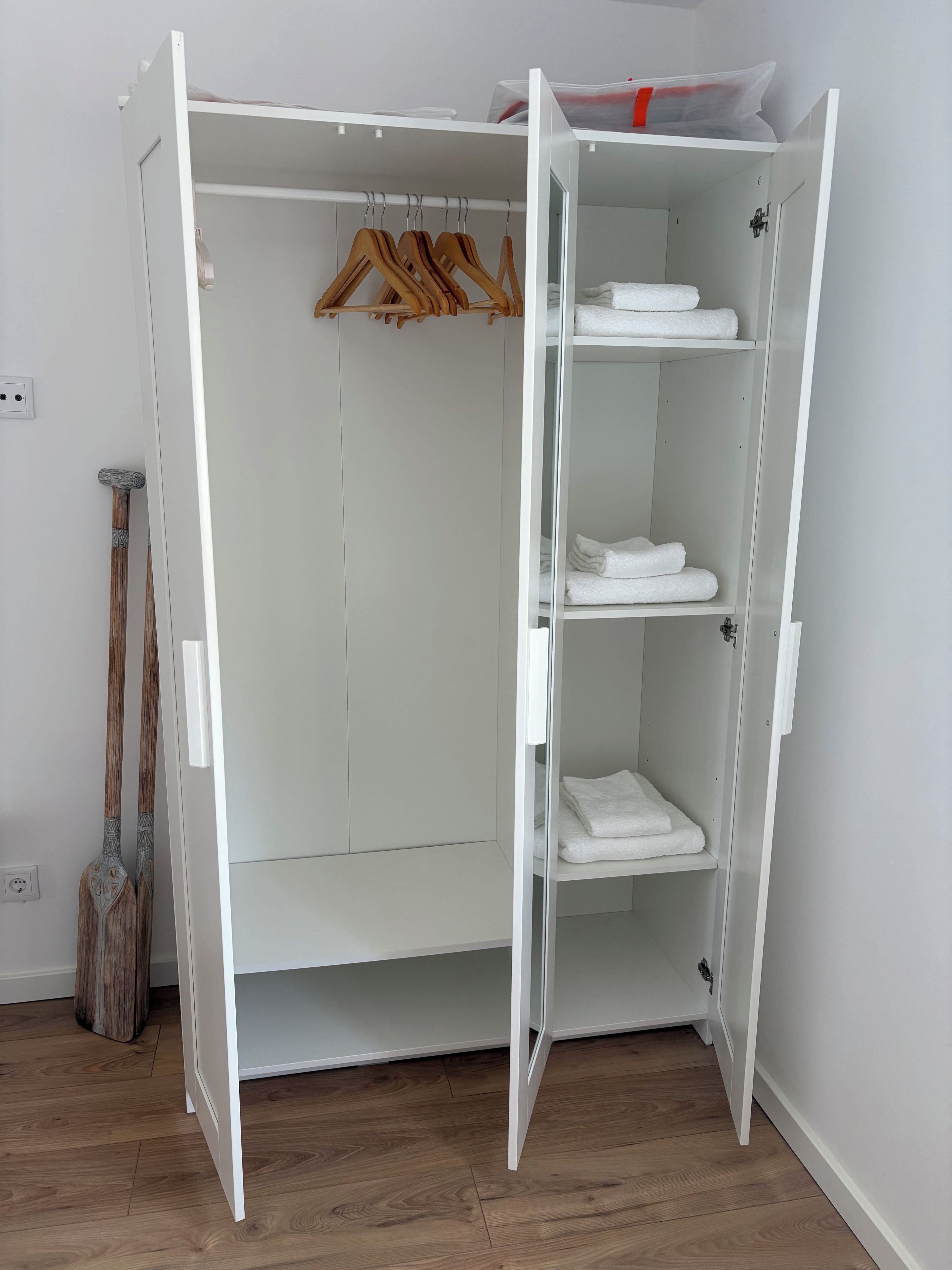 Ein weißer Kleiderschrank mit geöffneten Türen, Holzanziehern und ordentlich gefalteten weißen Handtüchern.