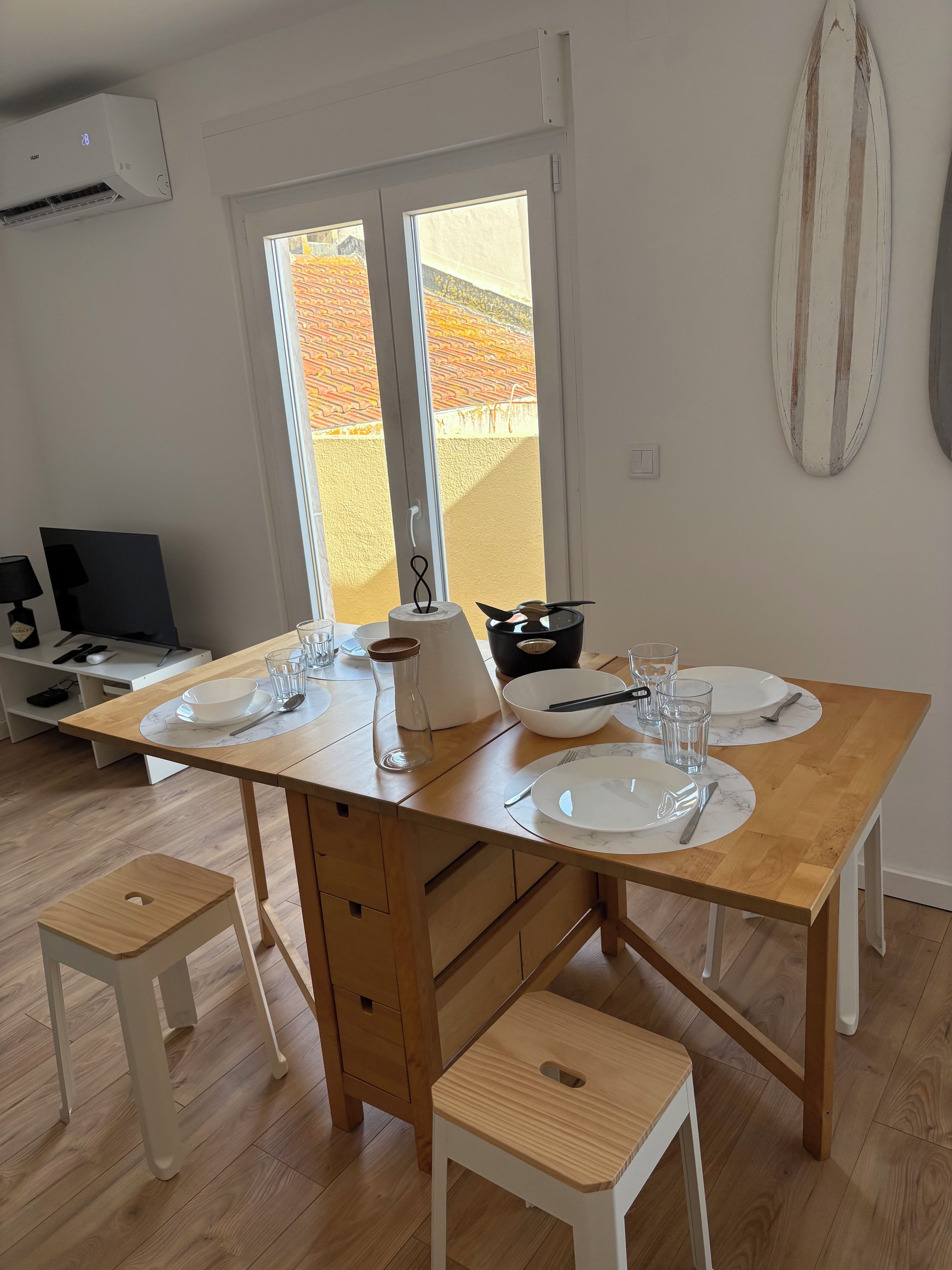 A modern kitchen with a dining table set for two, a coffee maker, and a view of a brick building outside.
