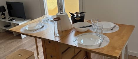 A modern kitchen with a dining table set for two, a coffee maker, and a view of a brick building outside.