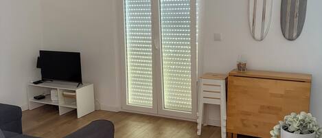 Un salon moderne avec un canapé gris, un meuble en bois et un téléviseur posé sur un meuble blanc.