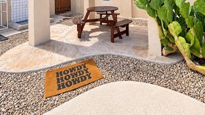 A covered patio area with a wooden table and benches, a cactus plant, and a doormat with the text 'HOWDY HOWDY'. - Desert Oasis w/ Private Pool Near ASU (Tempe)