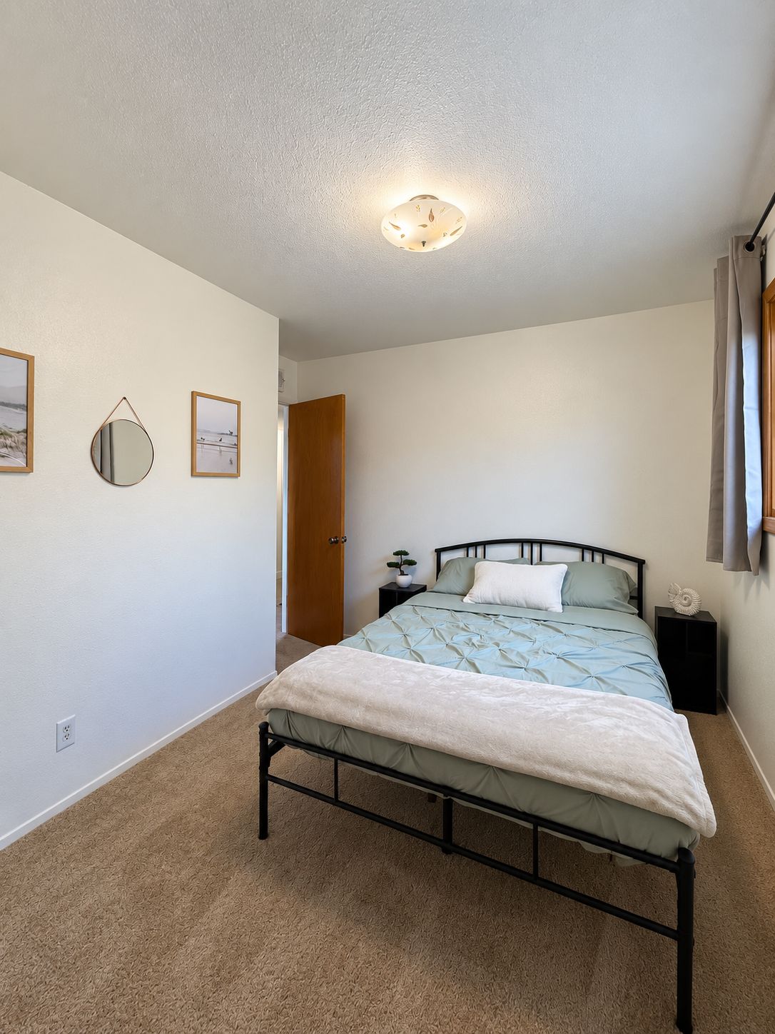 Quarto com cama, mesas de cabeceira, espelho fixado na parede e quadros emoldurados.