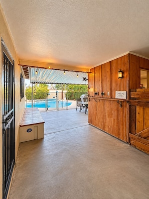 A covered outdoor area with a pool, a wooden wall, and a bench.