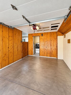 A spacious room with wooden paneling, a concrete floor, and a ceiling with exposed beams and lighting fixtures.