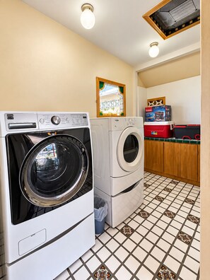 A laundry room with two front-loading washing machines, a tiled floor, and a wooden cabinet with a red toolbox.