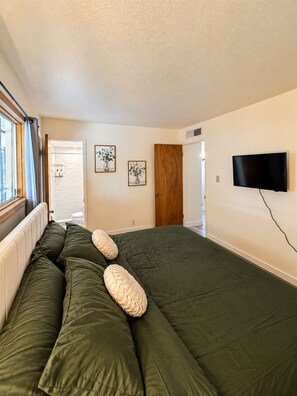 A bedroom with a large bed, a television mounted on the wall, and a window with curtains.